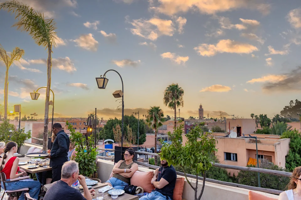 Diners on the Coco Rooftop terrace with the Koutoubia and evening sky beyond