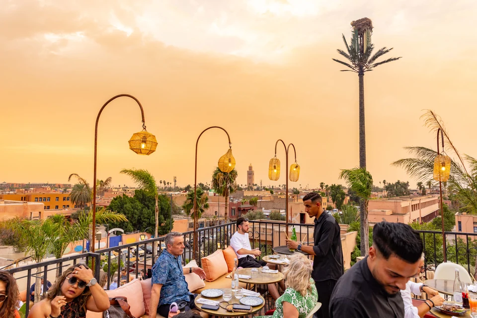 Waiter serving terrace guests beneath lanterns with a Koutoubia view